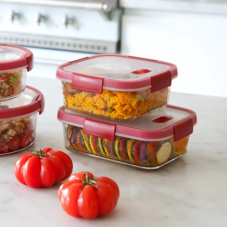 Dwa-prostokatne,-przezroczyste-pojemniki-z-czerwonymi-pokrywkami-ustawione-jeden-na-drugim-na-blacie-kuchennym,-w-srodku-makaron-i-warzywa-w-plastrach-obok-dwa-czerwone-pomidory,-widok-z-przodu..webp
