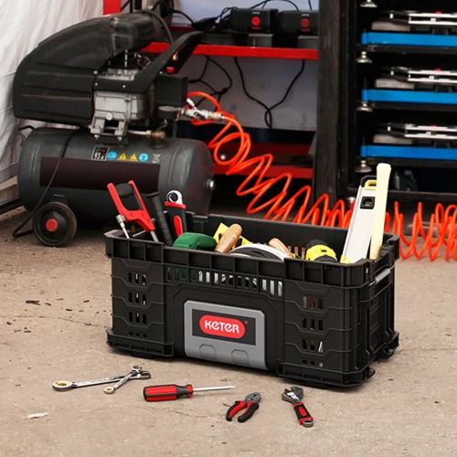 Kosz wypełniony narzędziami ręcznymi ustawiony na podłodze w warsztacie, wokół leżą luźne narzędzia.