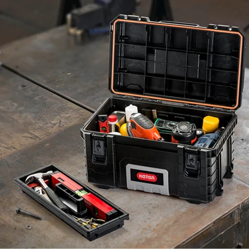 Otwarta skrzynka narzędziowa ustawiona na blacie roboczym, wypełniona narzędziami i akcesoriami, z wyjętą tacką z przegródkami; widok z góry z lekkim kątem.