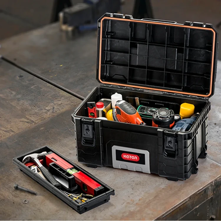 Otwarta skrzynka narzędziowa ustawiona na blacie roboczym, wypełniona narzędziami i akcesoriami, z wyjętą tacką z przegródkami; widok z góry z lekkim kątem.