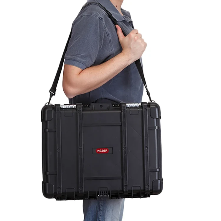 Mężczyzna w koszulce trzymający walizkę narzędziową na ramieniu za pomocą czarnego paska, widok z boku.