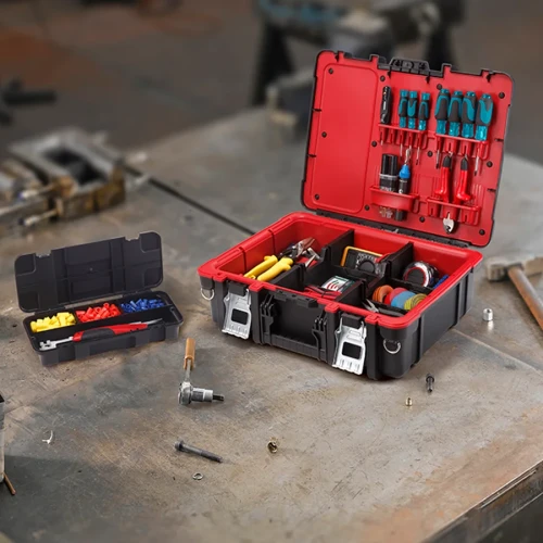 Walizka narzędziowa otwarta na metalowym blacie, wypełniona narzędziami i akcesoriami, obok mniejszy organizer z kolorowymi elementami.