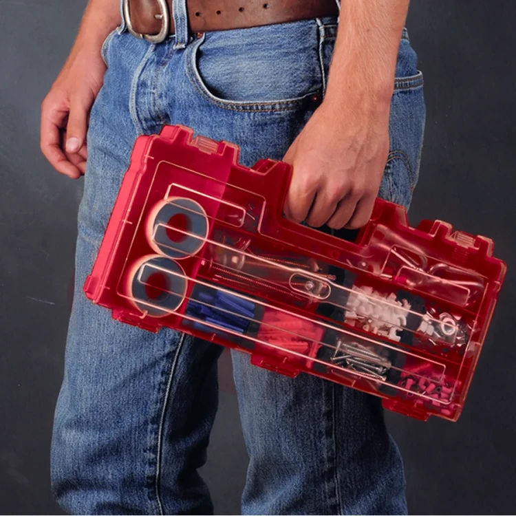 Zbliżenie na rękę trzymającą przezroczysty czerwony organizer z drobnymi elementami, takimi jak śrubki, taśmy i końcówki, widok z boku.