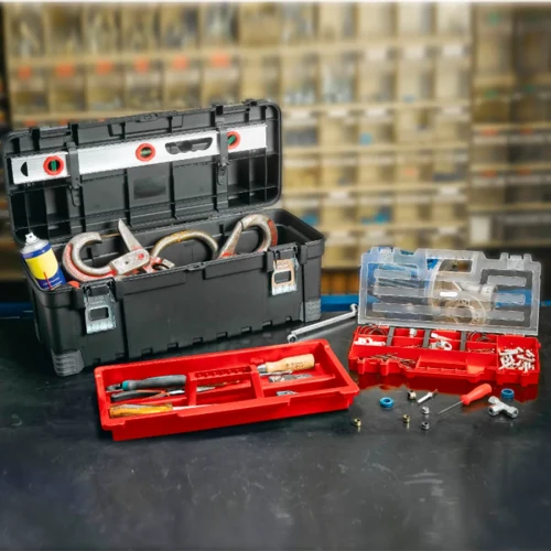 Otwarta skrzynka z widocznymi narzędziami i akcesoriami w środku, w tym poziomica w pokrywie i dwa organizery z przegródkami, ustawiona na blacie warsztatowym.