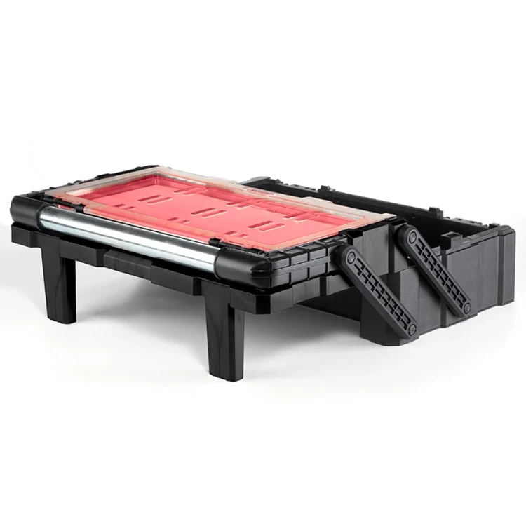 Czarno-czerwona skrzynka narzędziowa w pozycji rozłożonej na nóżkach; przezroczysta pokrywa odsłania puste miejsce na przegródki.