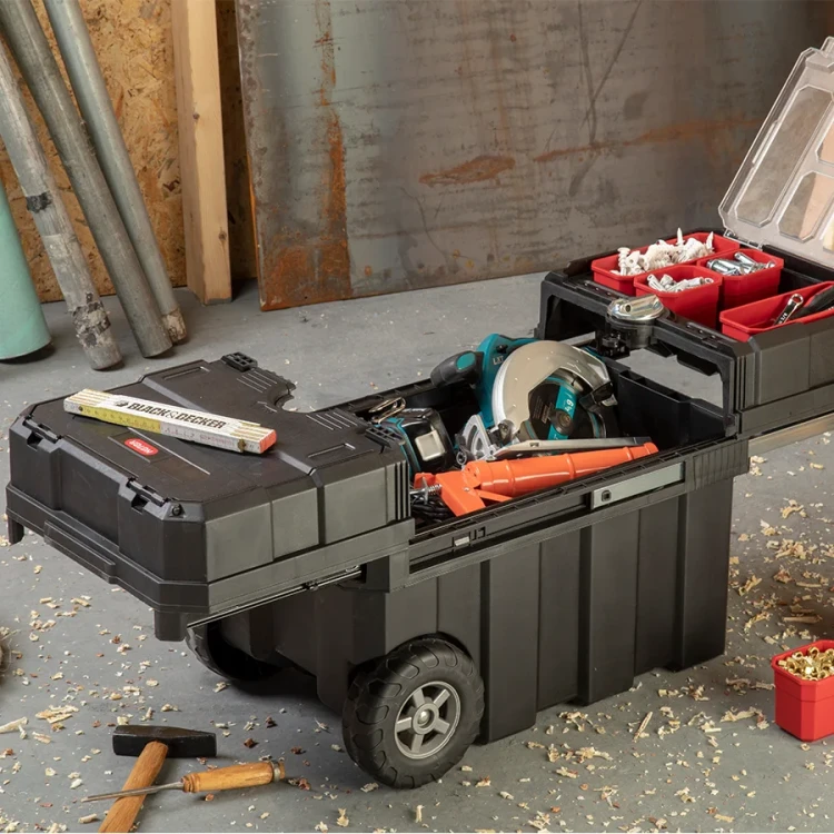 Skrzynka narzędziowa w kolorze czarnym z rozłożoną górną częścią na prowadnicy, widoczne czerwone pojemniki z drobnymi elementami, elektronarzędzia i akcesoria stolarskie.