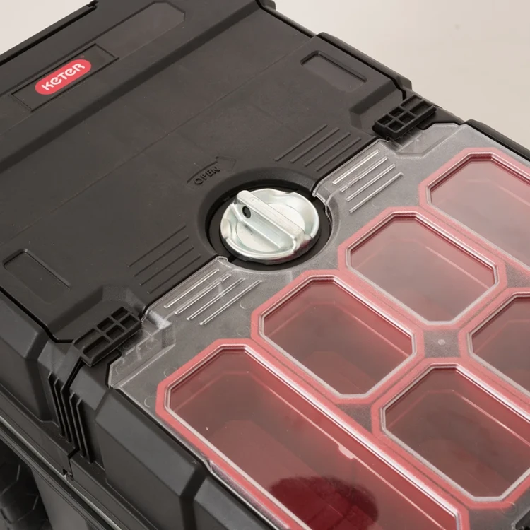 Widok z góry na zamkniętą skrzynkę z przezroczystą pokrywą z sześcioma czerwonymi przegrodami oraz dużym srebrnym pokrętłem zamykającym pośrodku.