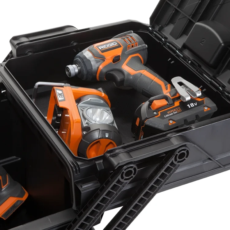 Widok wnętrza skrzynki z narzędziami – w środku widać latarkę, wkrętarkę i baterię, wszystkie w czarno-pomarańczowej kolorystyce.