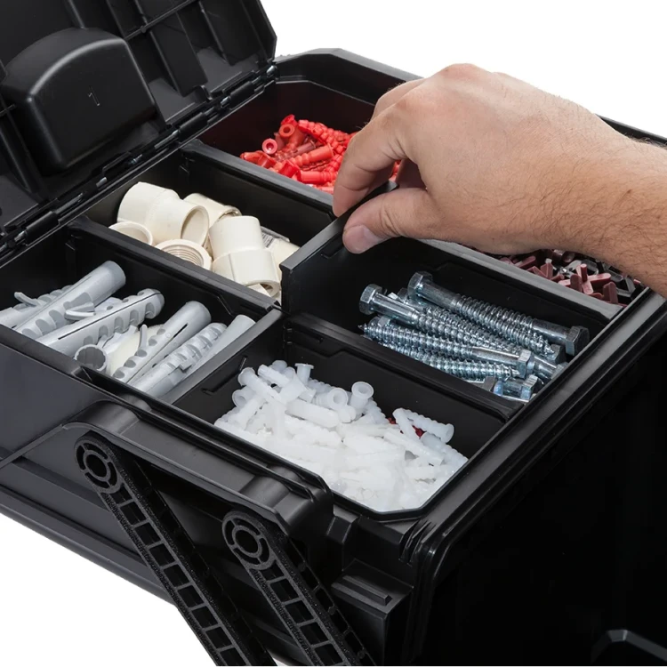 Skrzynka otwarta, wypełniona różnymi kołkami i śrubami; dłoń sięga po element z jednej z przegród.