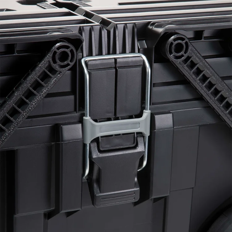 Zbliżenie na metalowy zatrzask skrzynki; solidny mechanizm zamykający umieszczony centralnie między podwójnymi ramionami zawiasowymi.