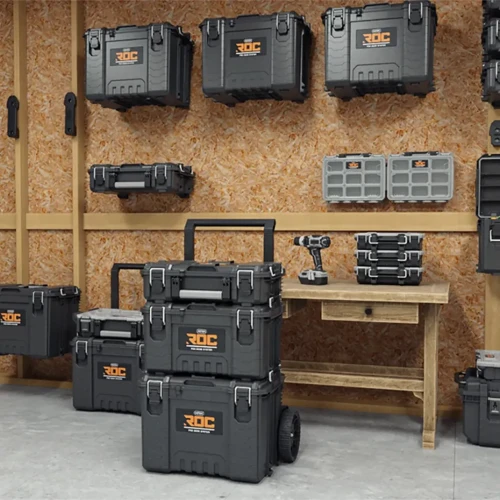 Widok na pomieszczenie warsztatowe z czarnymi skrzyniami narzędziowymi na kółkach i do zawieszenia, ustawionymi na ścianie i podłodze przy drewnianym stole.